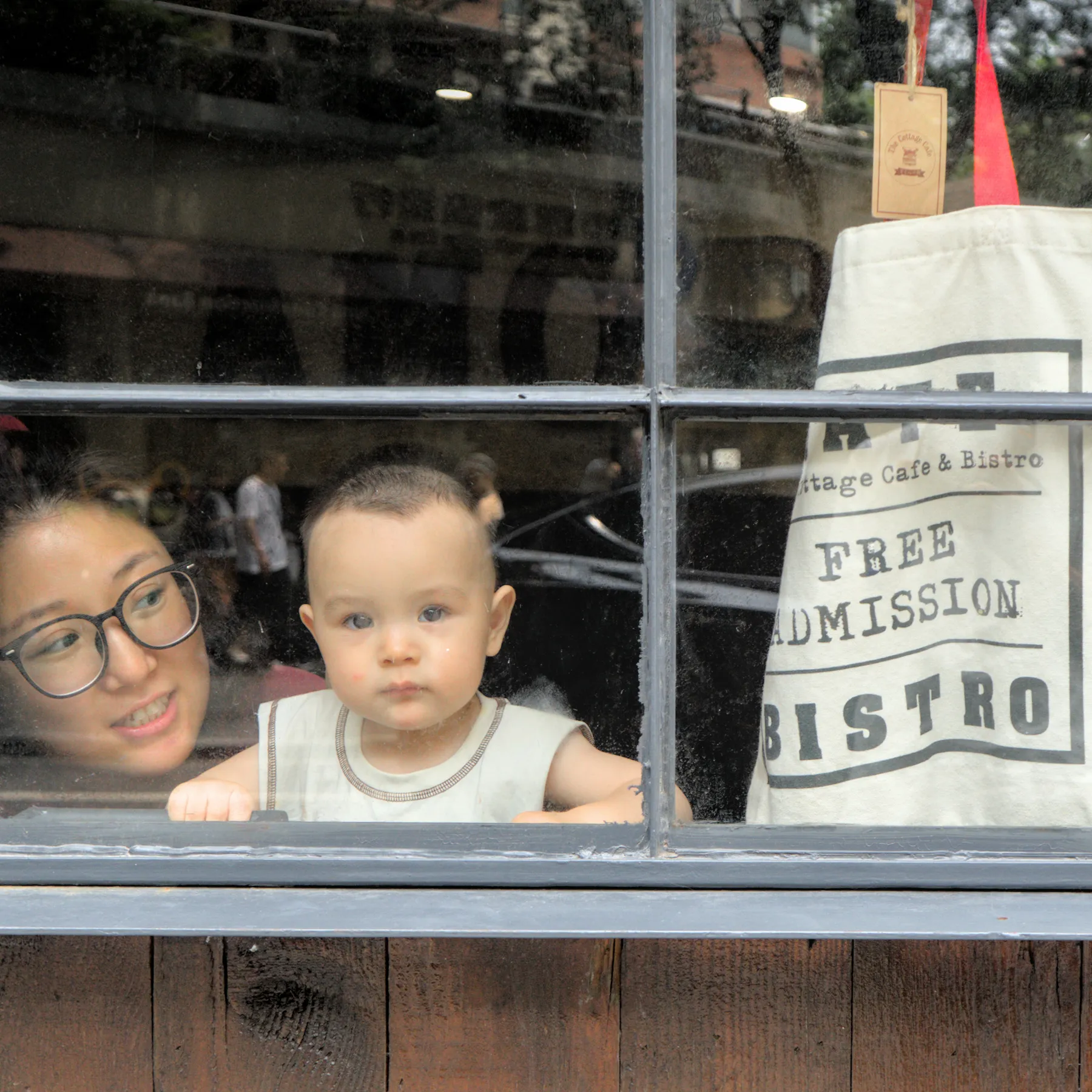A boy and his mother looking out the window of a café, square aspect ratio