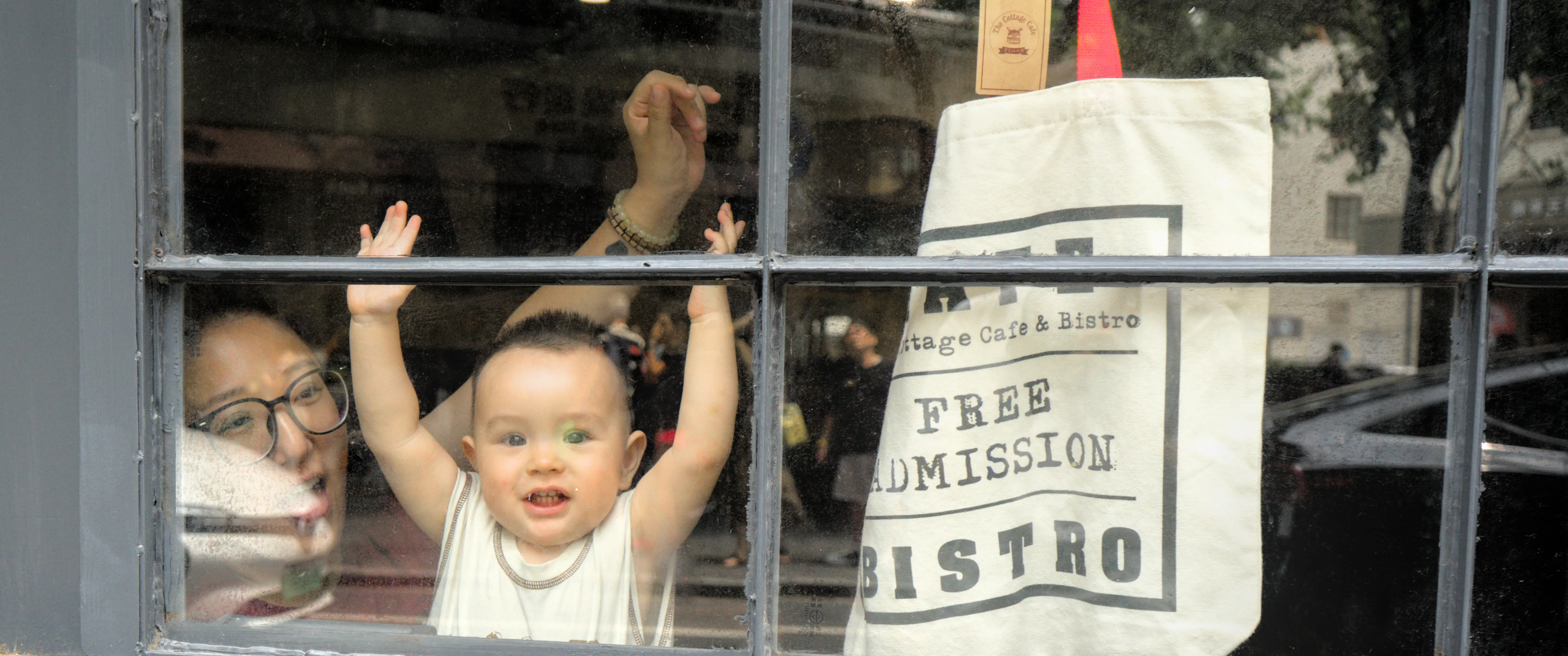 A baby boy behind a café window with his arms in the air