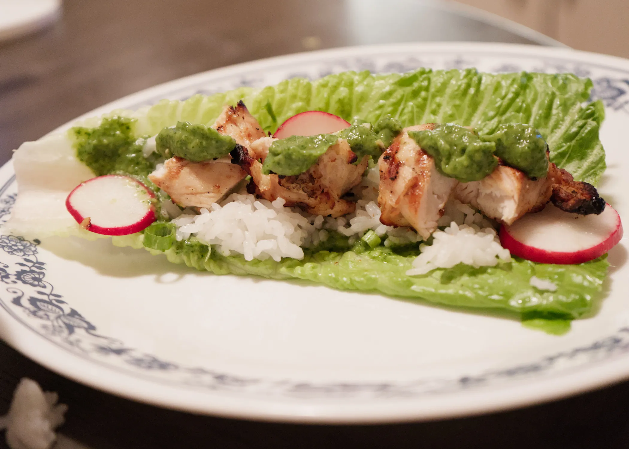 A chicken lettuce wrap with rice, guacamole, and radishes