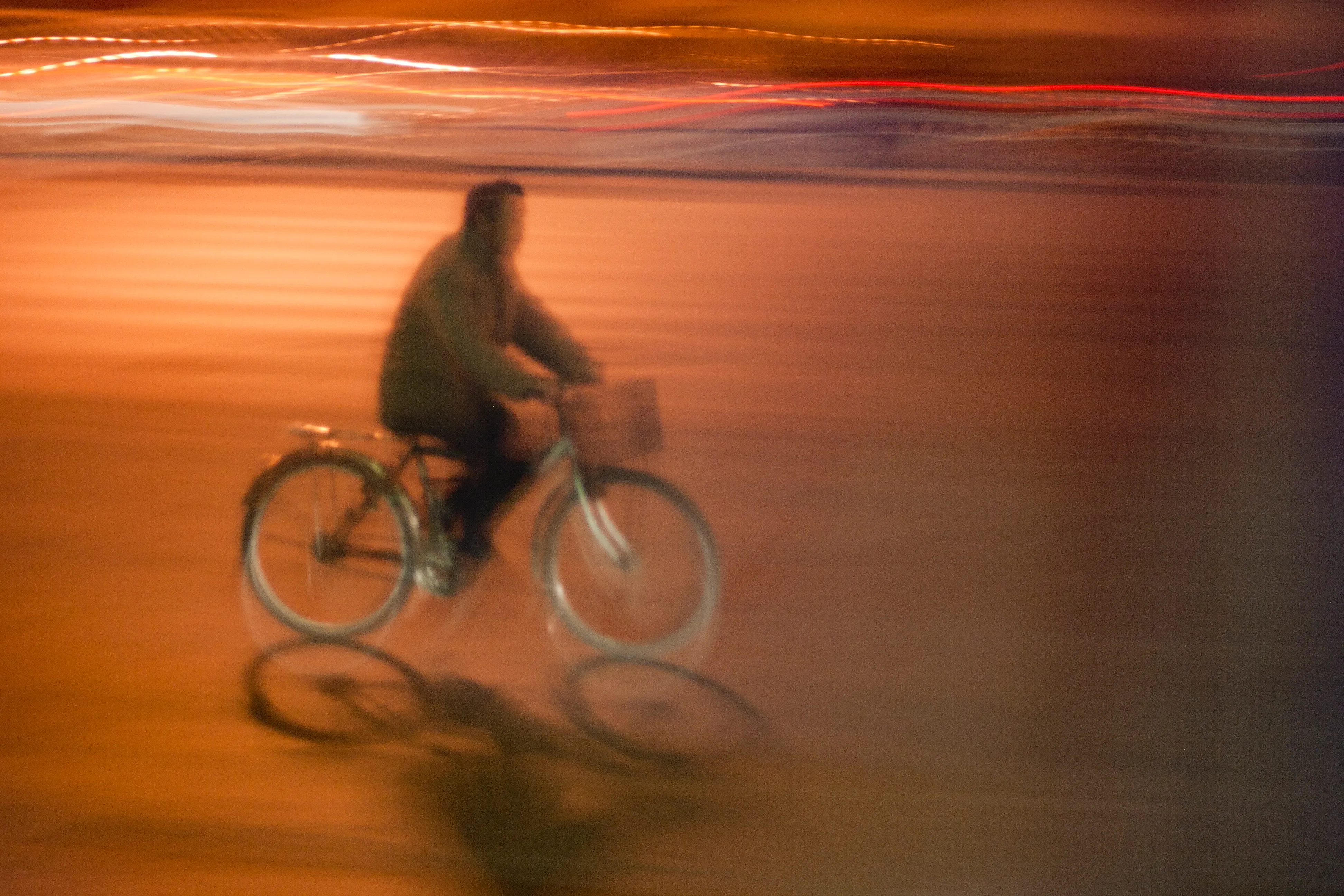 A bicyclist rides through a Beijing street at night while the background smears into orange streaks.