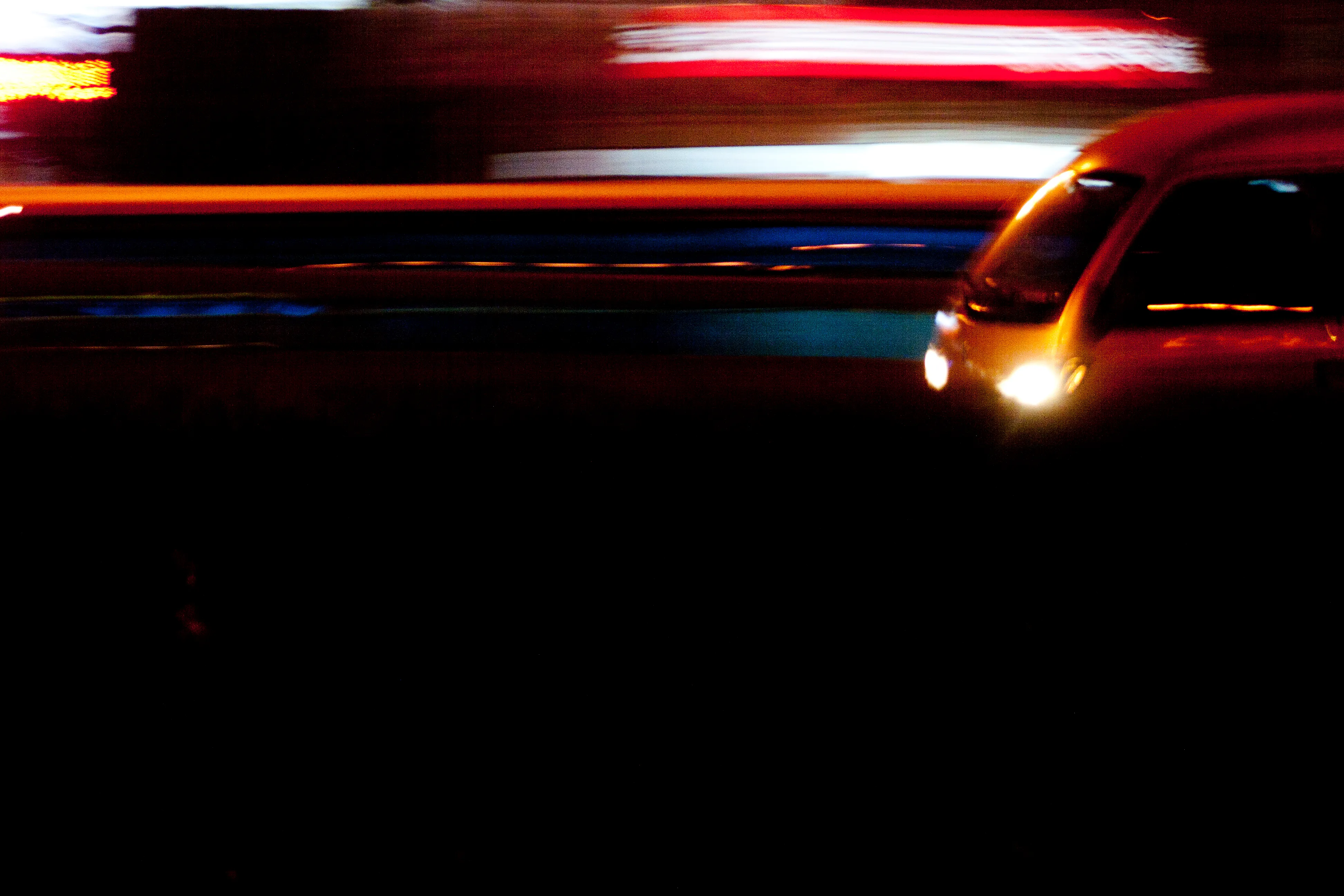 A vehicle at night streaks across the frame in horizontal bands of red, white, and amber light.