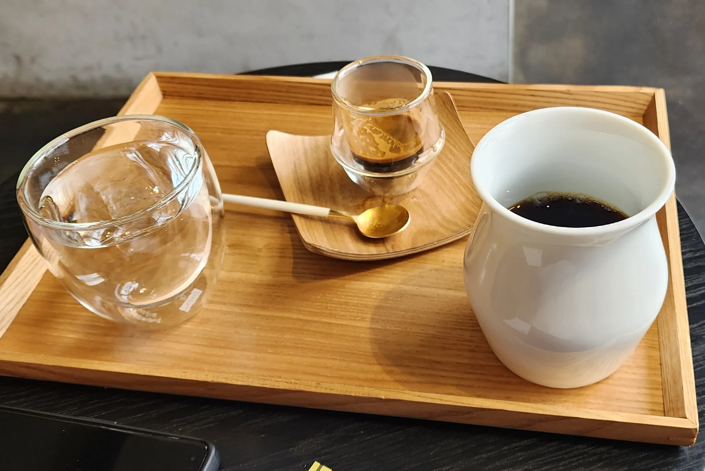 a wooden tray with a glass of water, a cup of espresso, and a cup of pourover coffee on it