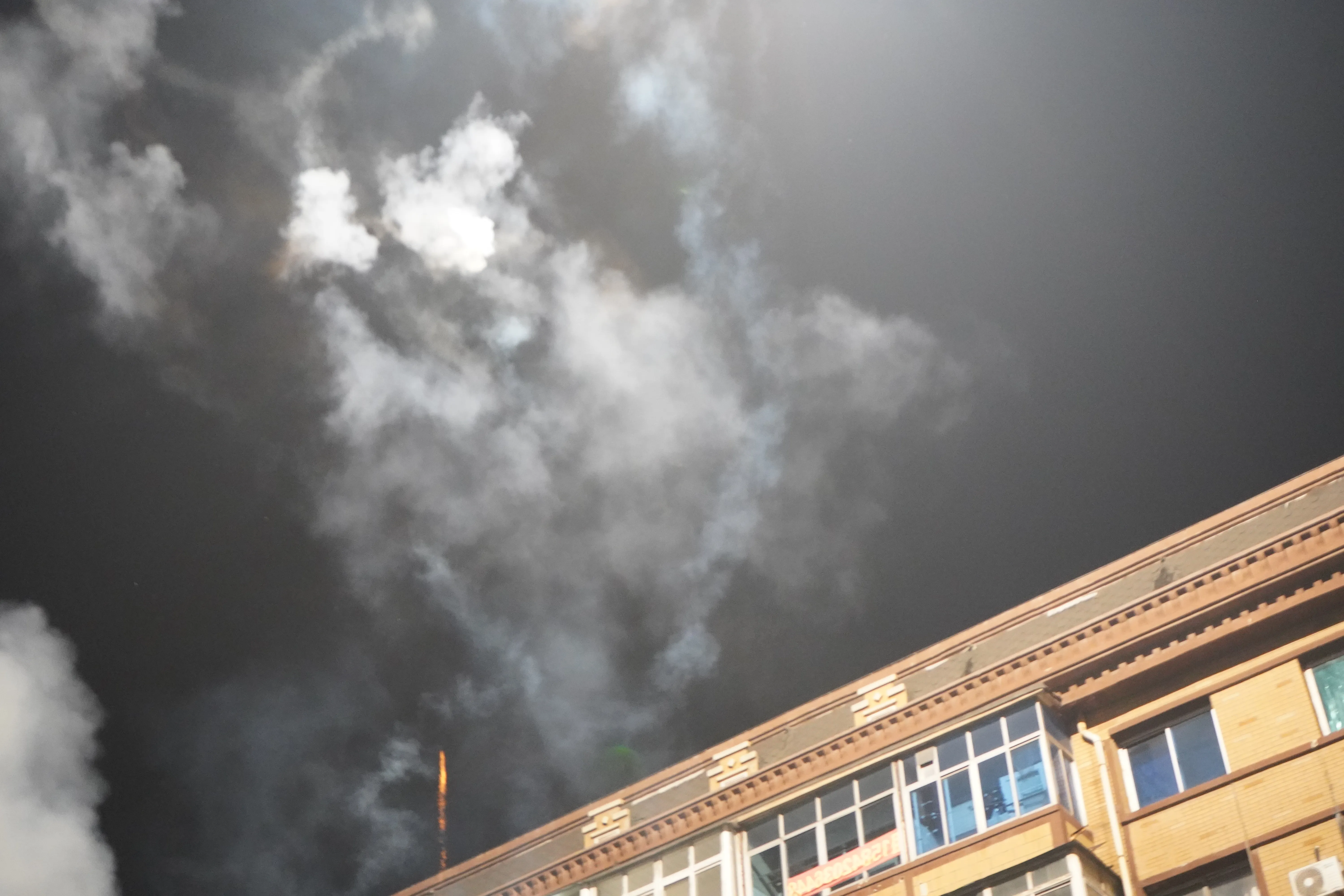 Colorful fireworks bursting high above six-story apartment buildings, briefly turning the night sky bright.