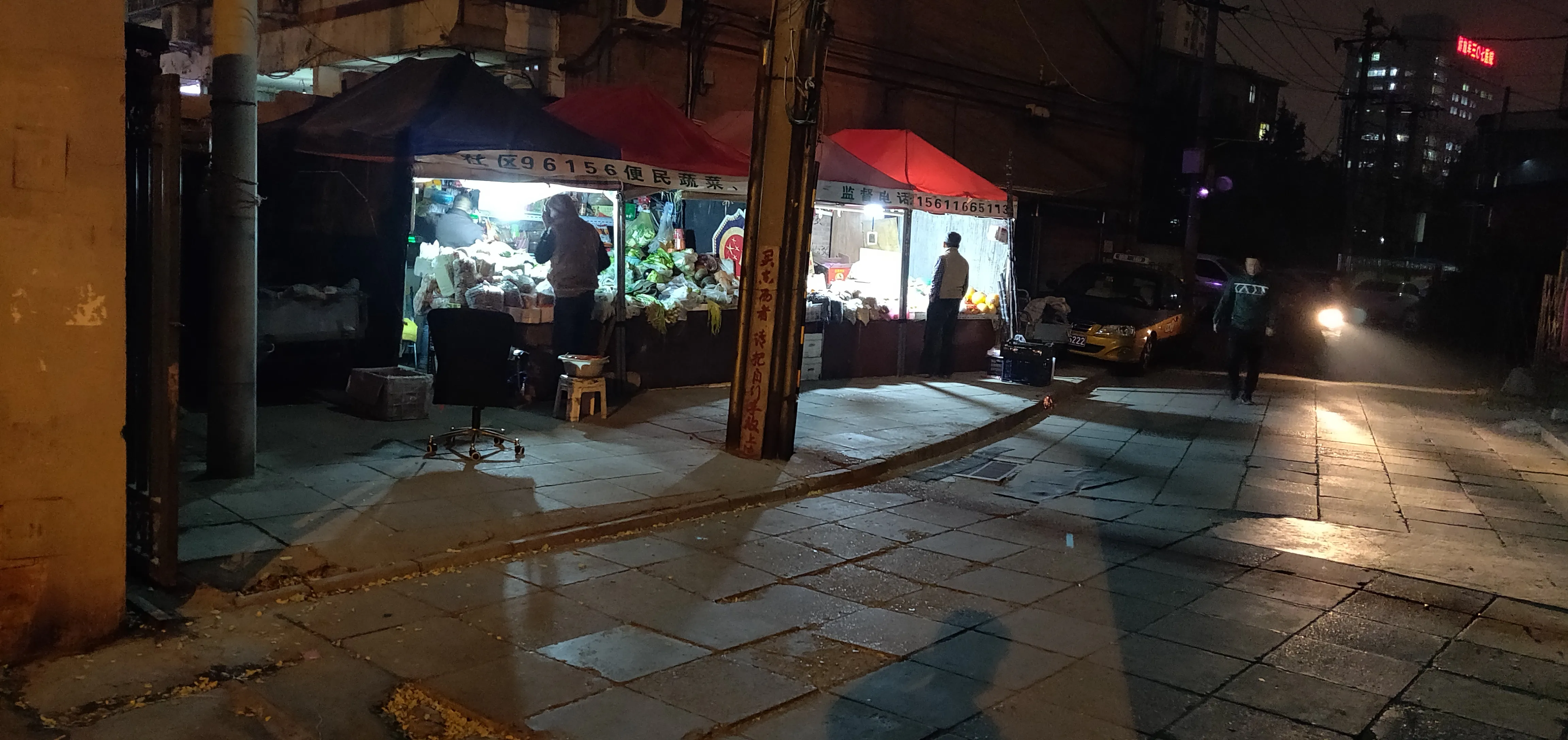 Produce stalls under tents on a Beijing city sidewalk at night.