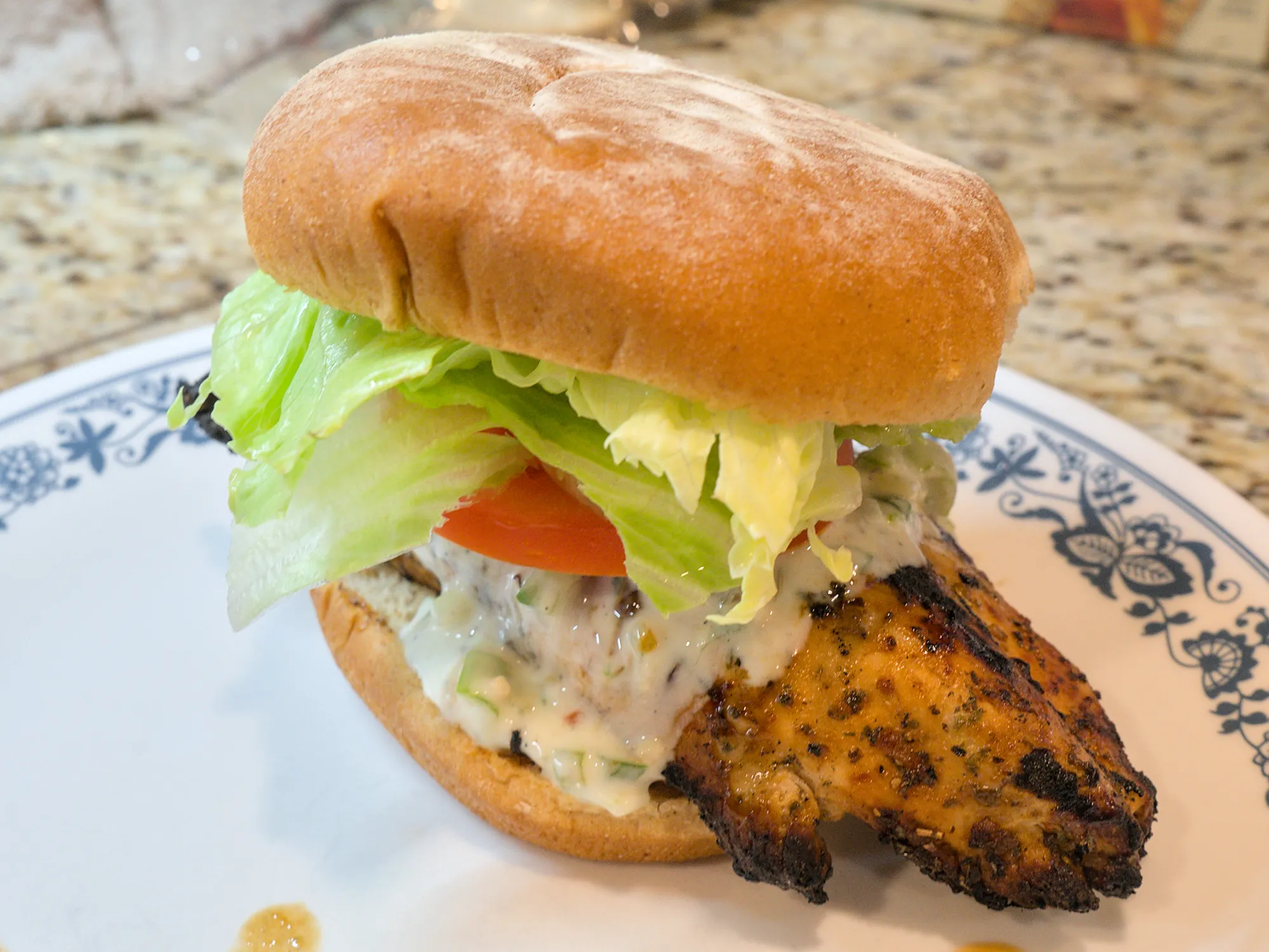 A chicken sandwich with lettuce, tomatoes, and tzatziki sauce